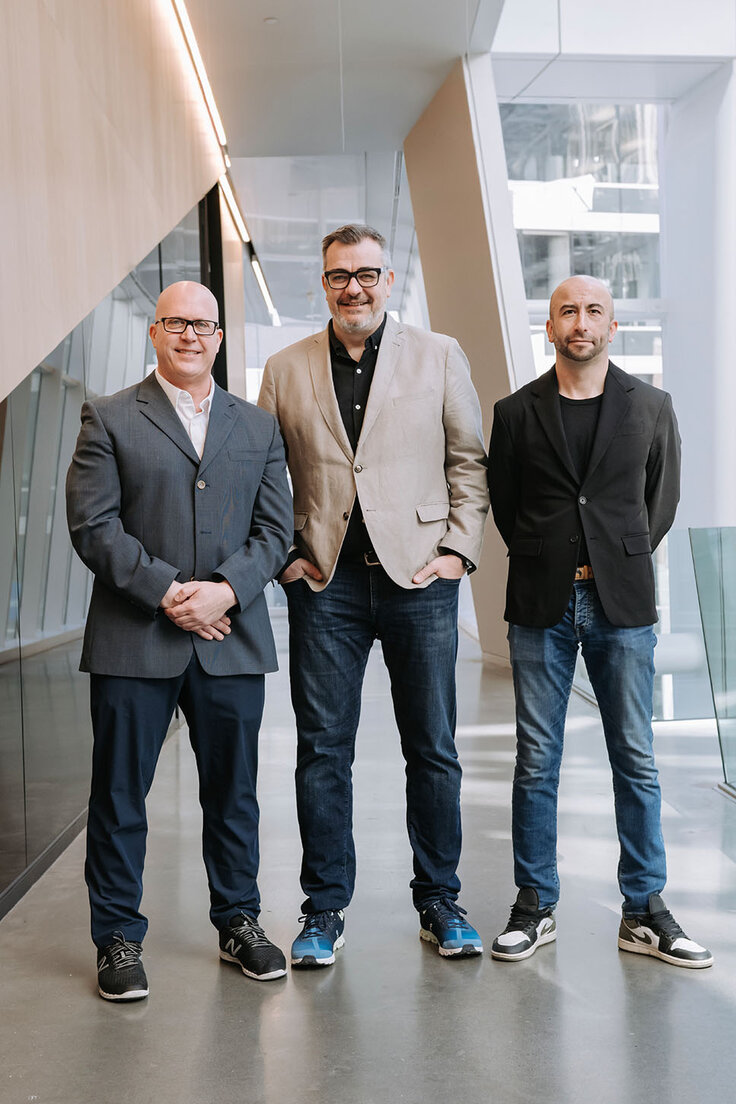 Three people standing in an indoor glass-enclosed space at HEC Montréal.