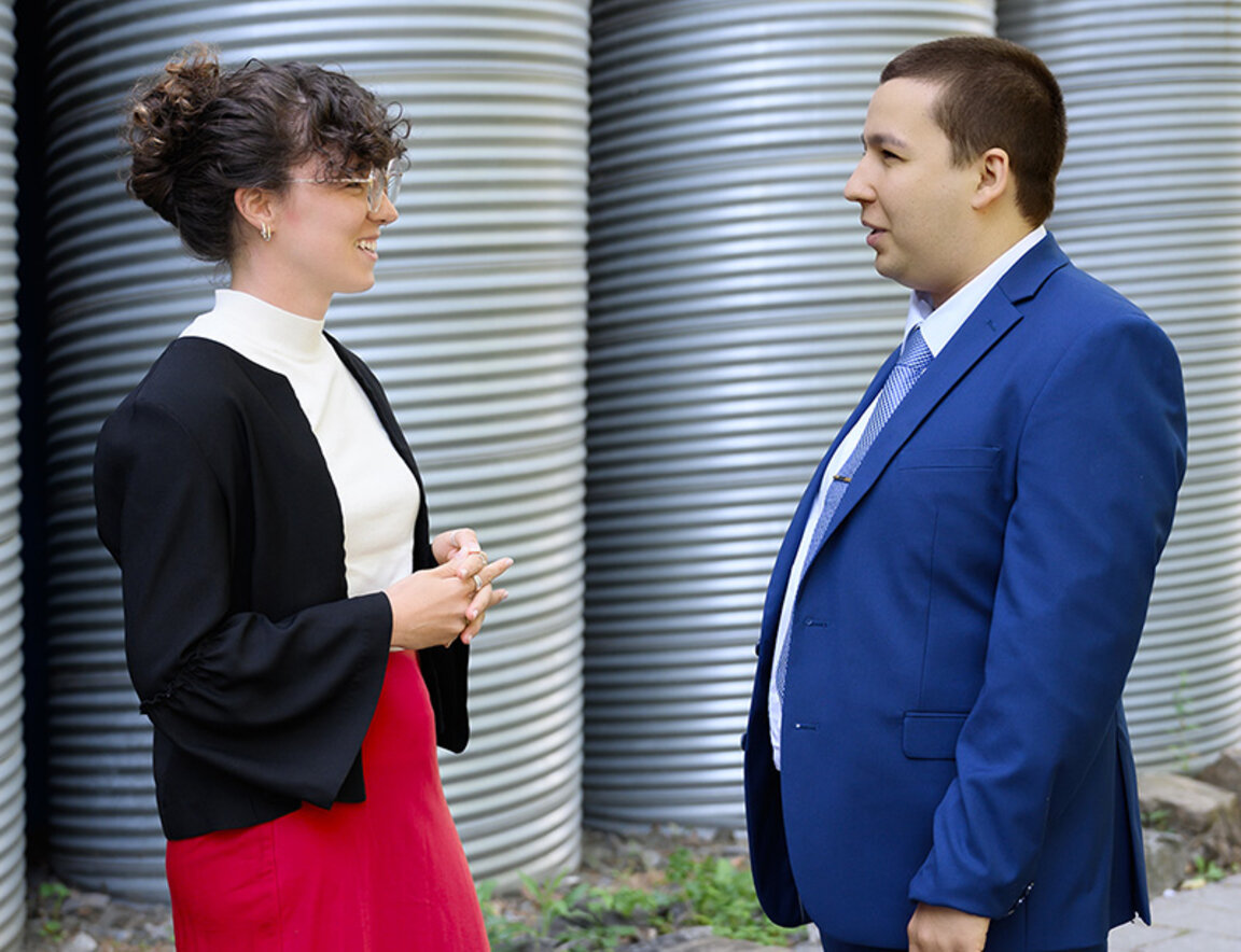 Une étudiante et un étudiant du troisième cycle se tiennent debout l’une face à l’autre, à l’extérieur de HEC Montréal.