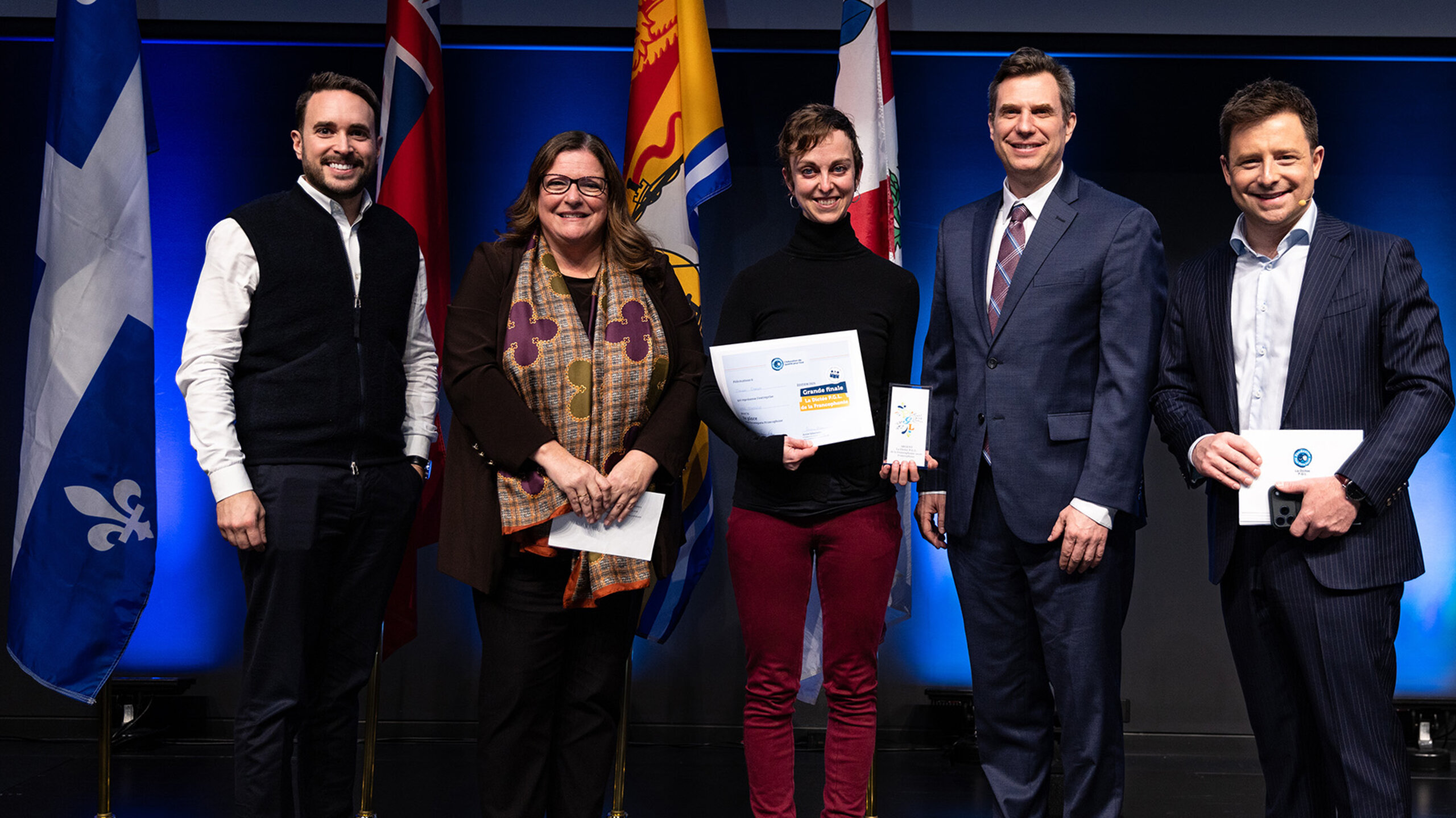 Cinq personnes posent sur scène lors de la finale de la Dictée P.G.L. de la Francophonie à HEC Montréal.