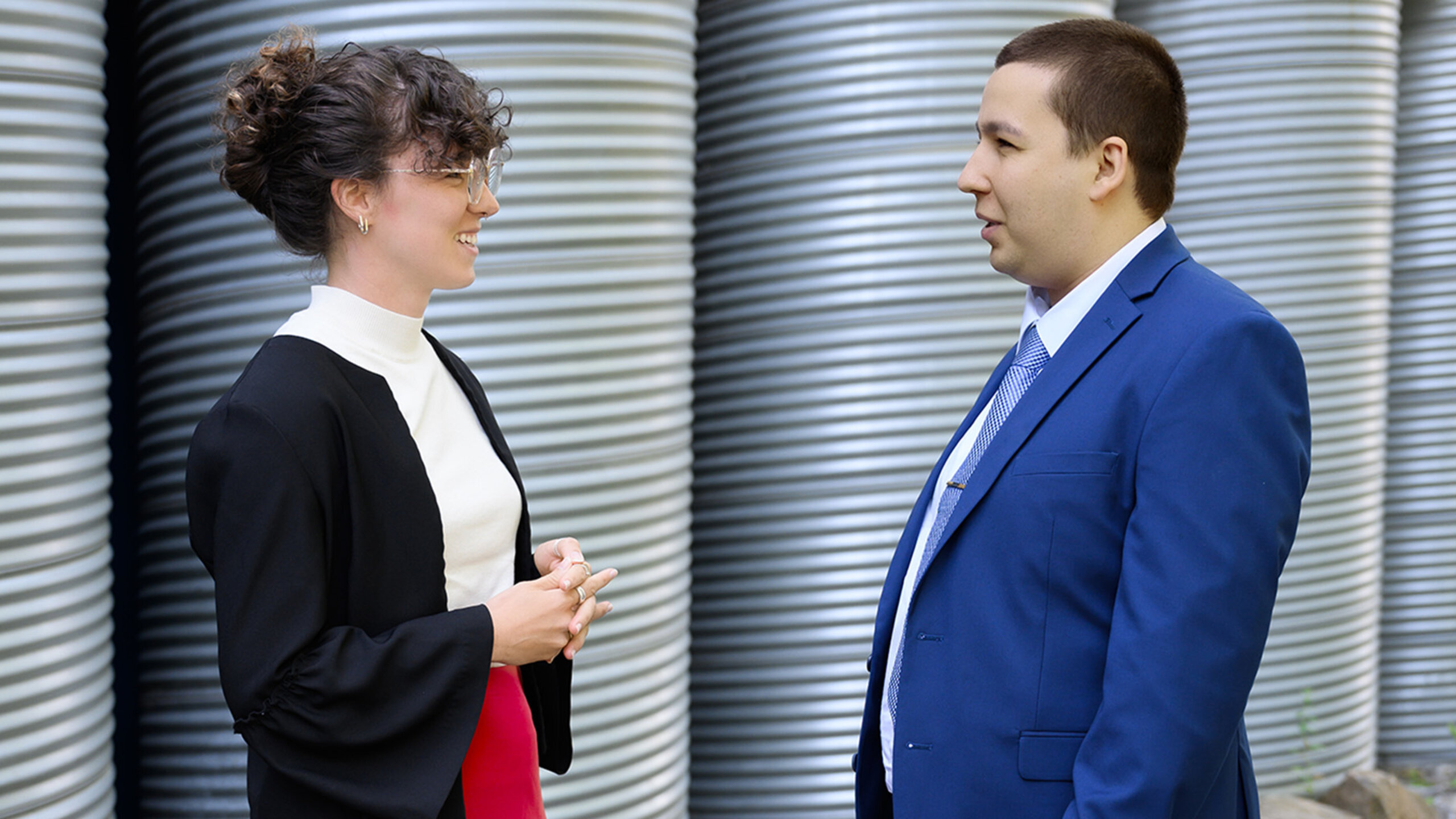 Une étudiante et un étudiant du troisième cycle se tiennent debout l’une face à l’autre, à l’extérieur de HEC Montréal.