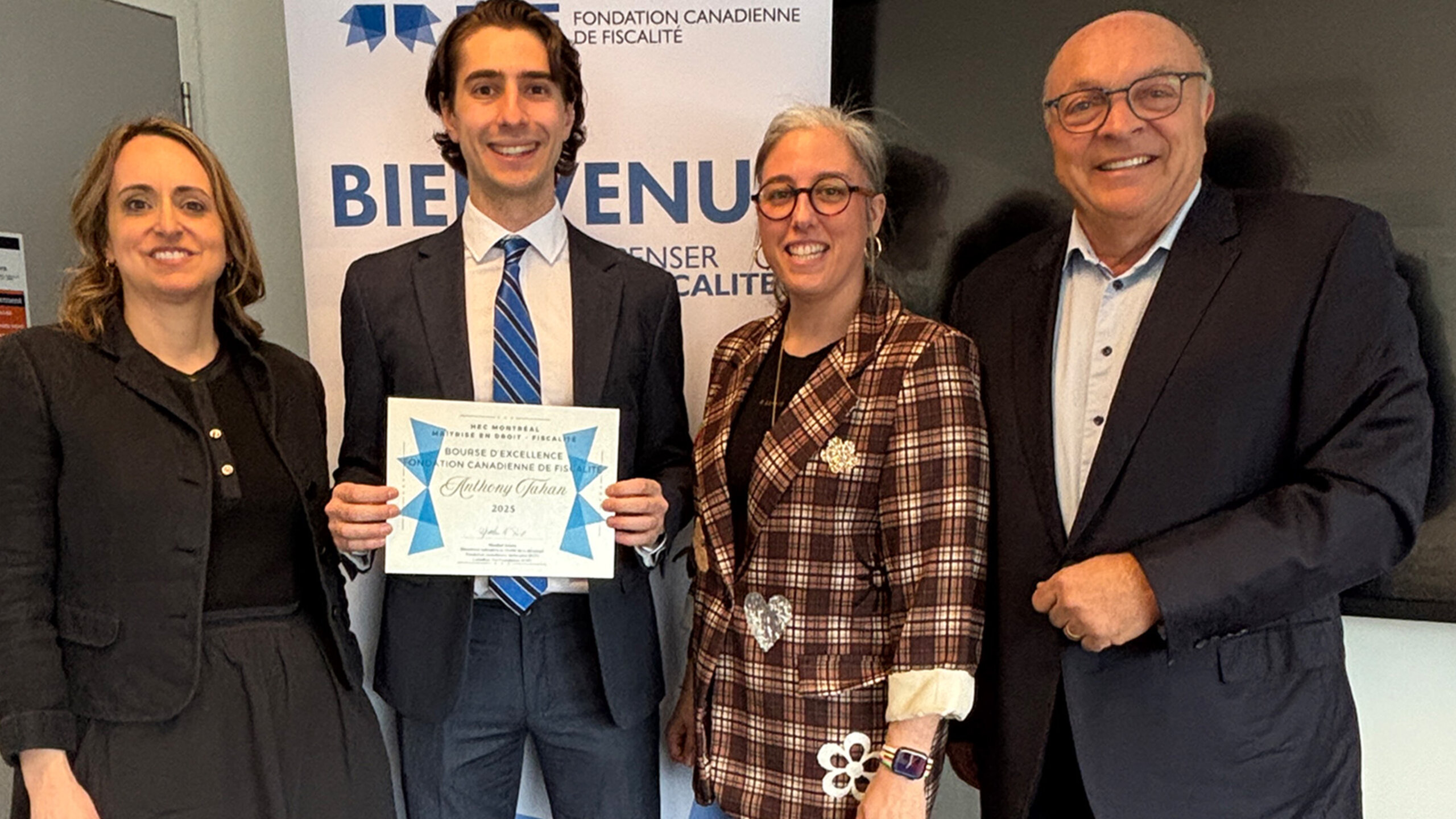 Le diplômé Anthony Tahan tenant un certificat, entouré de trois personnes, devant une bannière de la Fondation canadienne de fiscalité. 