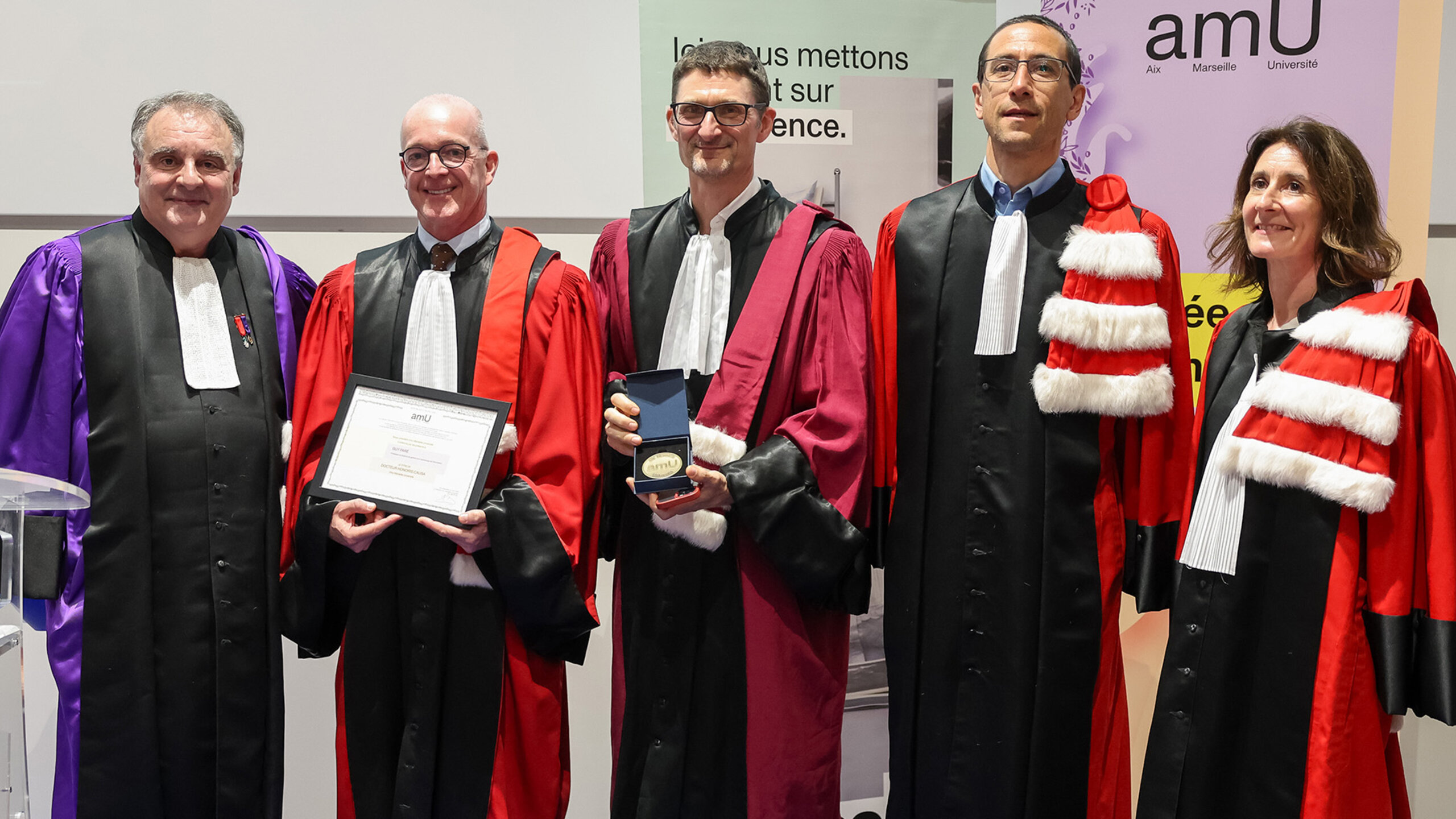 Cinq universitaires vêtus de toges se tenant debout, parmi lesquels Guy Paré, tenant un certificat.