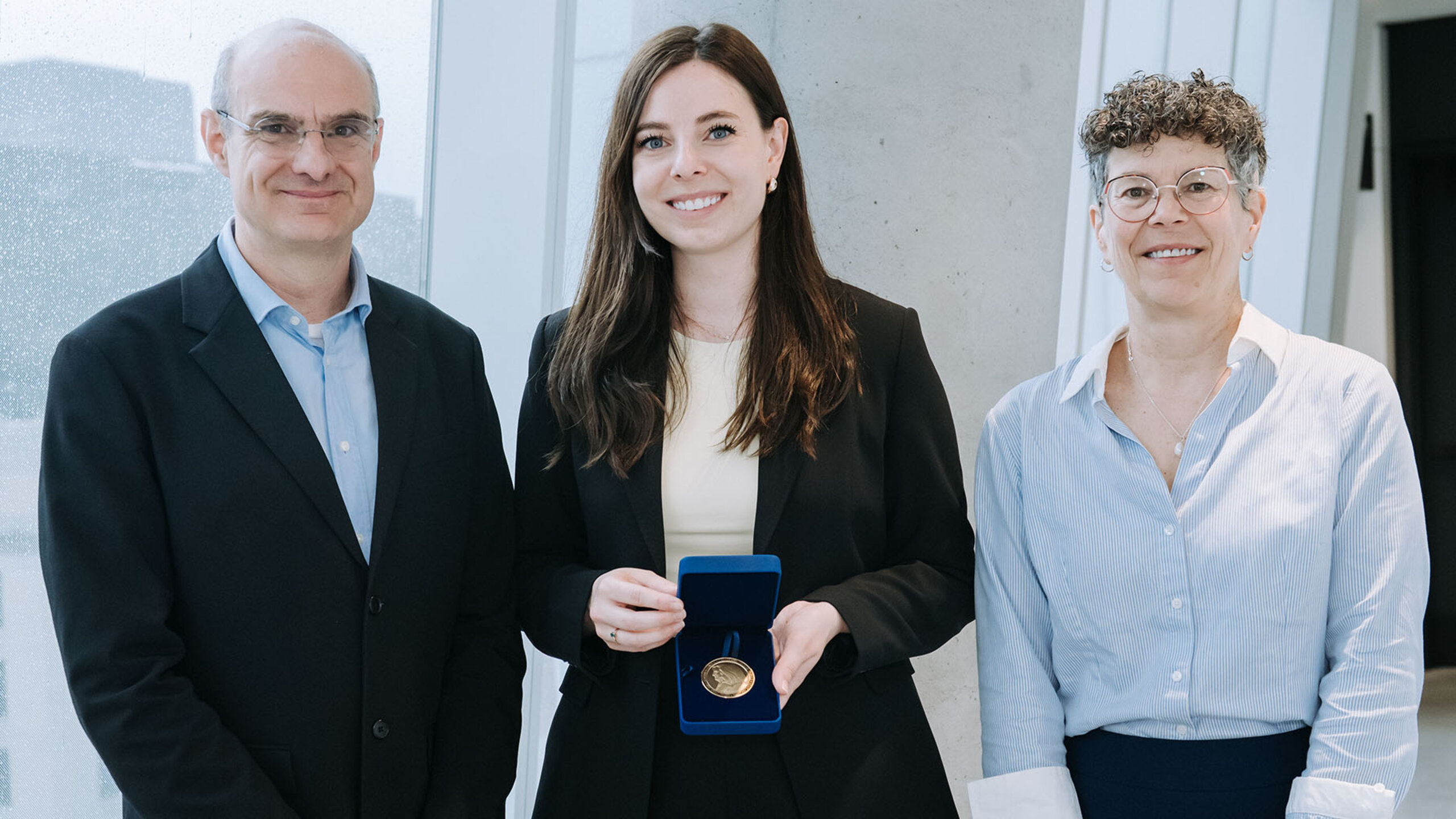 Federico Pasin, Sara-Maude Poirier et Johanne Turbide posent dans un corridor lumineux, Sara-Maude Poirier présentant une médaille dans un écrin ouvert.