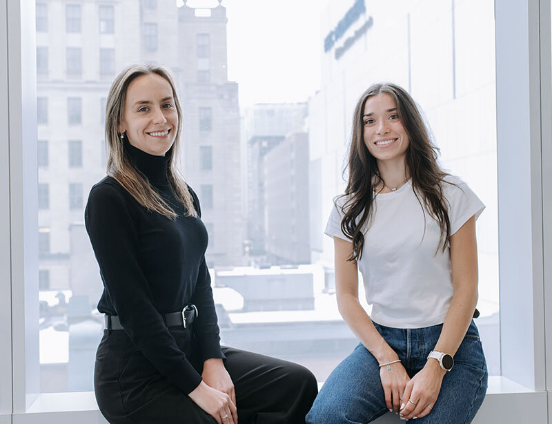 Deux personnes sont assises sur le rebord d’une grande fenêtre dans un espace intérieur de HEC Montréal, au centre-ville.
