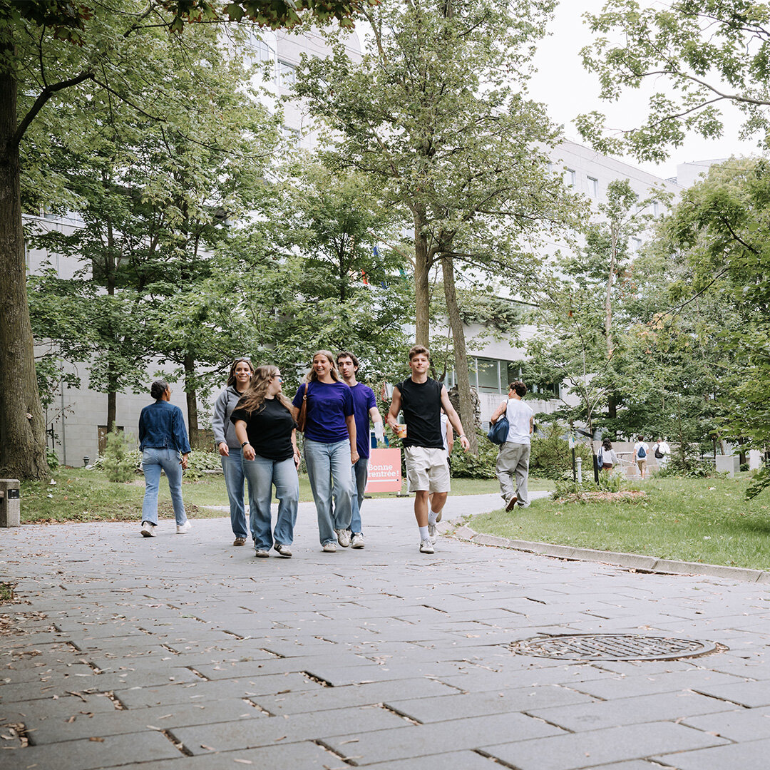 A group of students walking outside at the entrance to the campus.