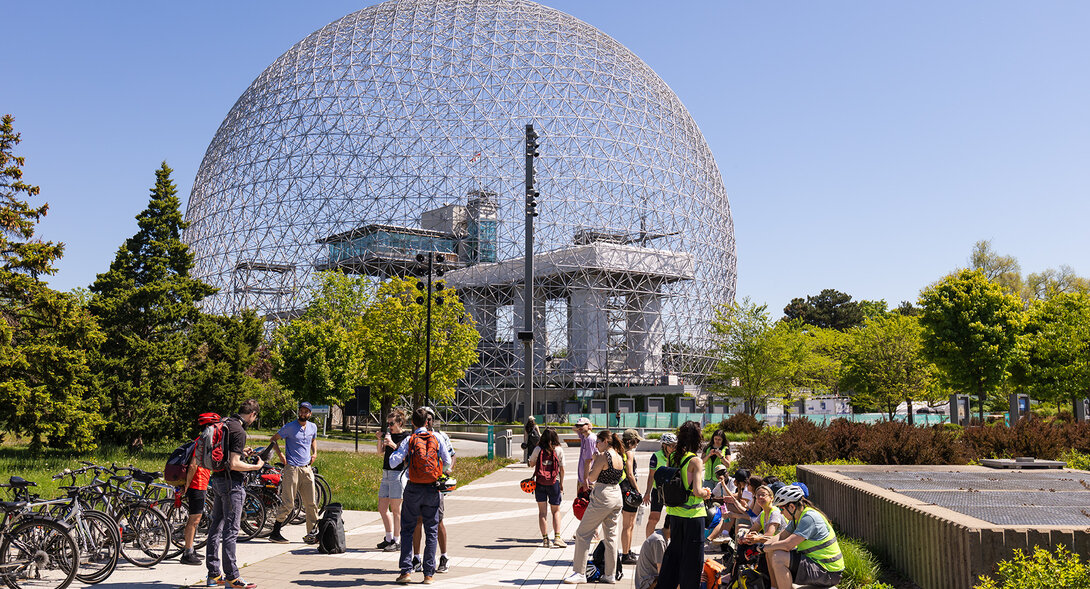 A group of students on bicycles participating in an educational activity in front of the Montreal Biosphere.