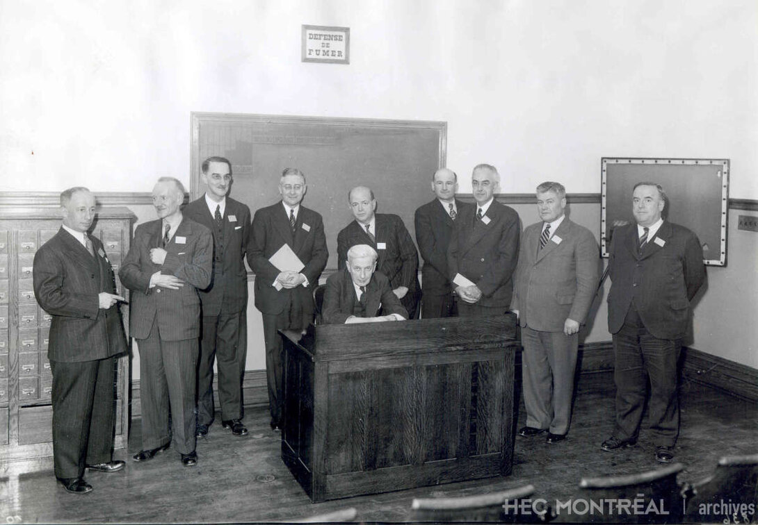   Description :  Édouard Montpetit et les étudiants de la troisième promotion de HEC dans une salle de classe. Date : 1915 Crédit photo : Photographe inconnu Cote archivistique : P005/XPH-0012