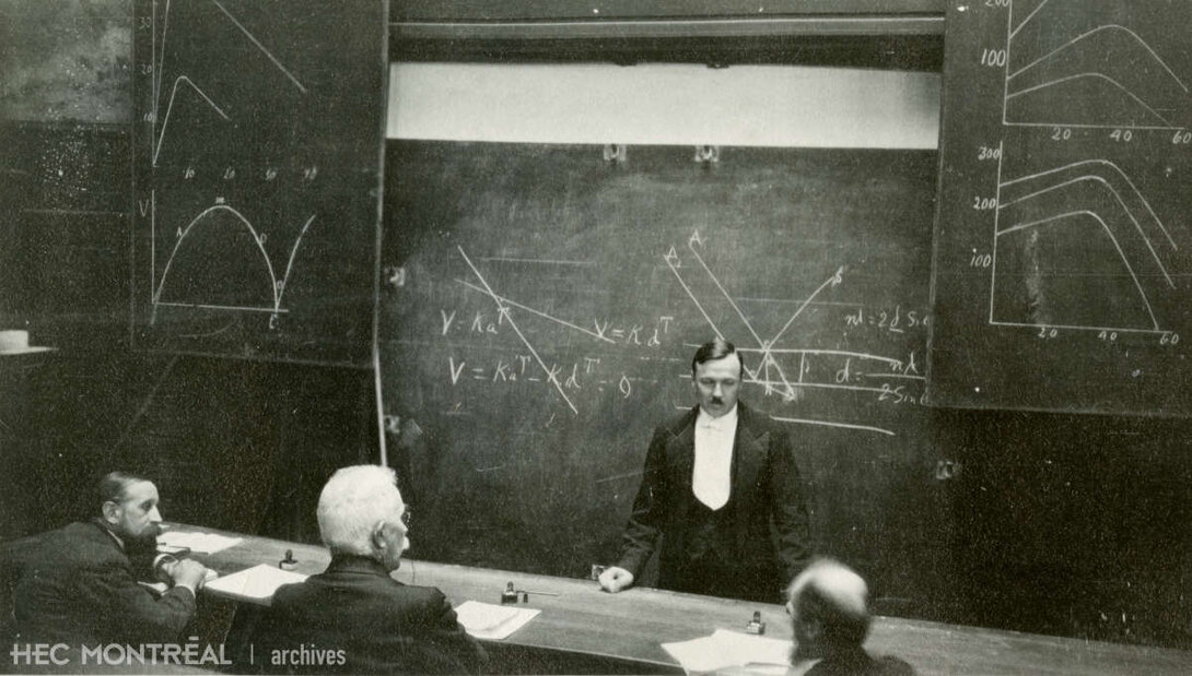   Description : Jean-Paul Riou discute avec des collègues dans une salle de cours. Date : ca 1920 Crédit photo : Photographe inconnu Cote archivistique : P042/X99,0001
